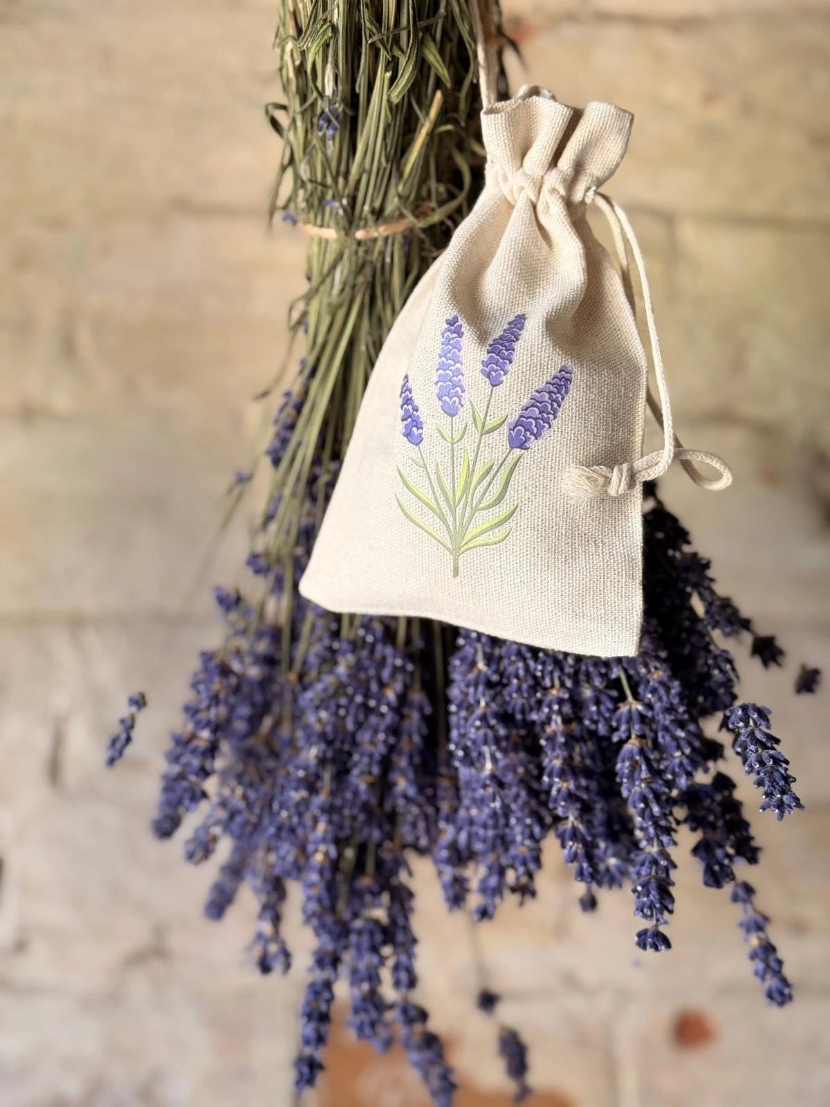 Lavender flowers hanging and dried lavender in a drawstring bag with lavender design on a white brick background