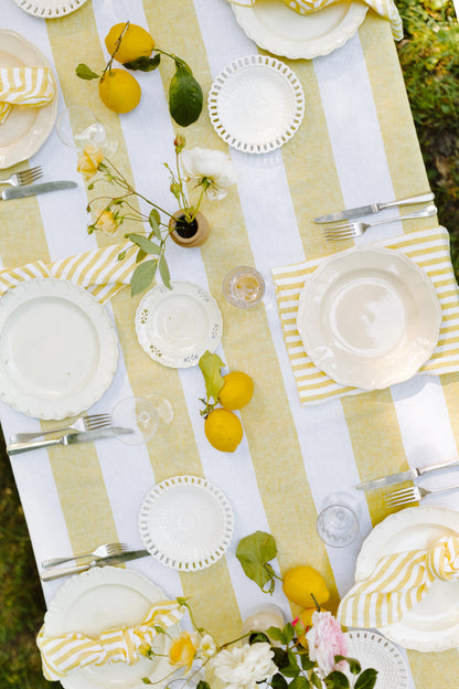 Outdoor table setting with yellow and white stripe tablecloth, plates, lemons, and flowers.
